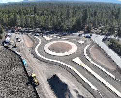 Aerial view of a new roundabout under construction at S Century Dr. & Huntington Rd. in a forested area.